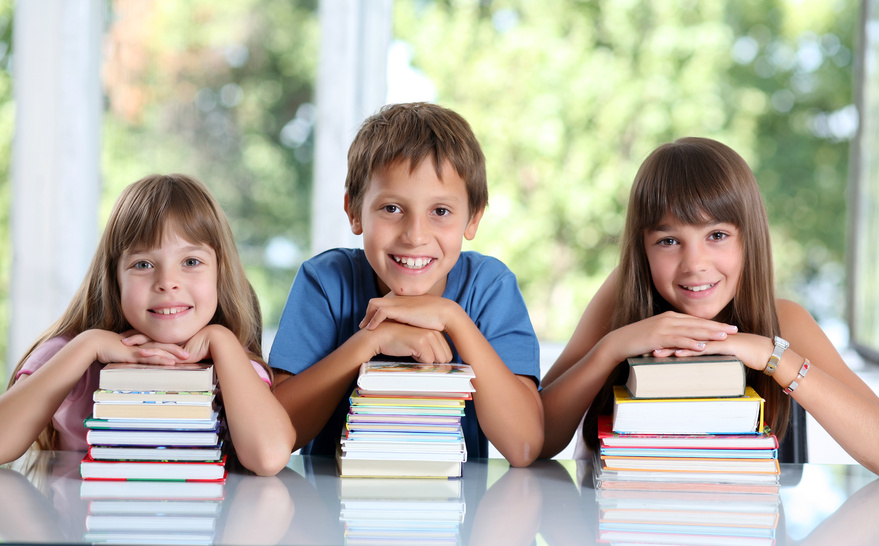 Glückliche Schulkinder mit vielen Büchern sitzend im Klassenzimmer